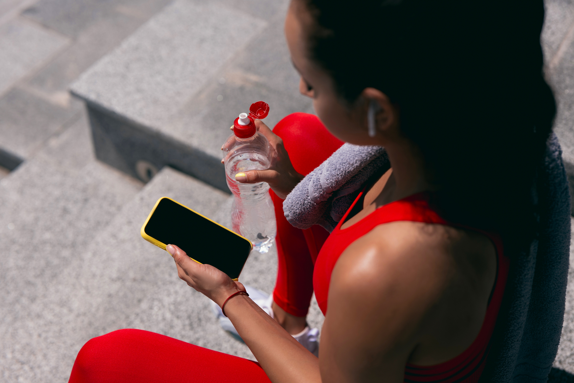 Woman with Dark Hair in Red Sportswear and water bottle checking her phone