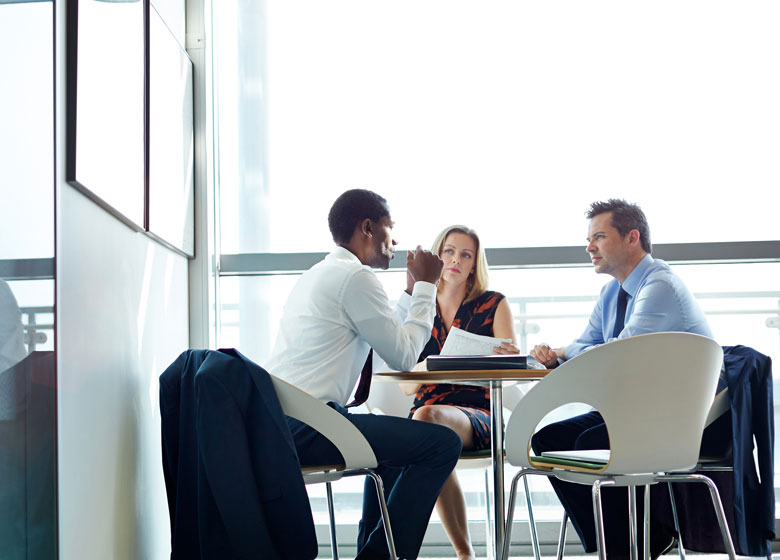 A trio of colleagues meet around an office table to discuss a deal.
