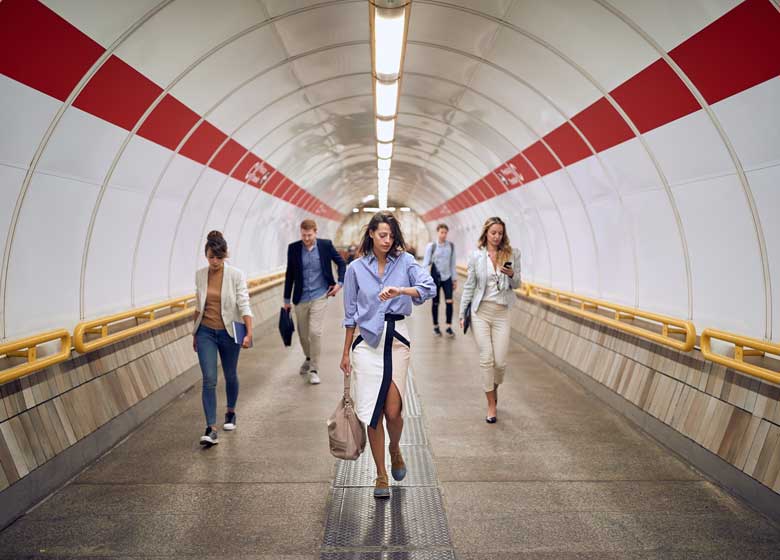 A group of busy commuters race forward through a subway tunnel