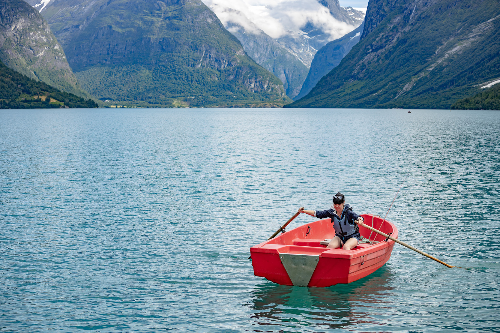 Woman in a red boat in the ocean in front of mountains on a rising tide