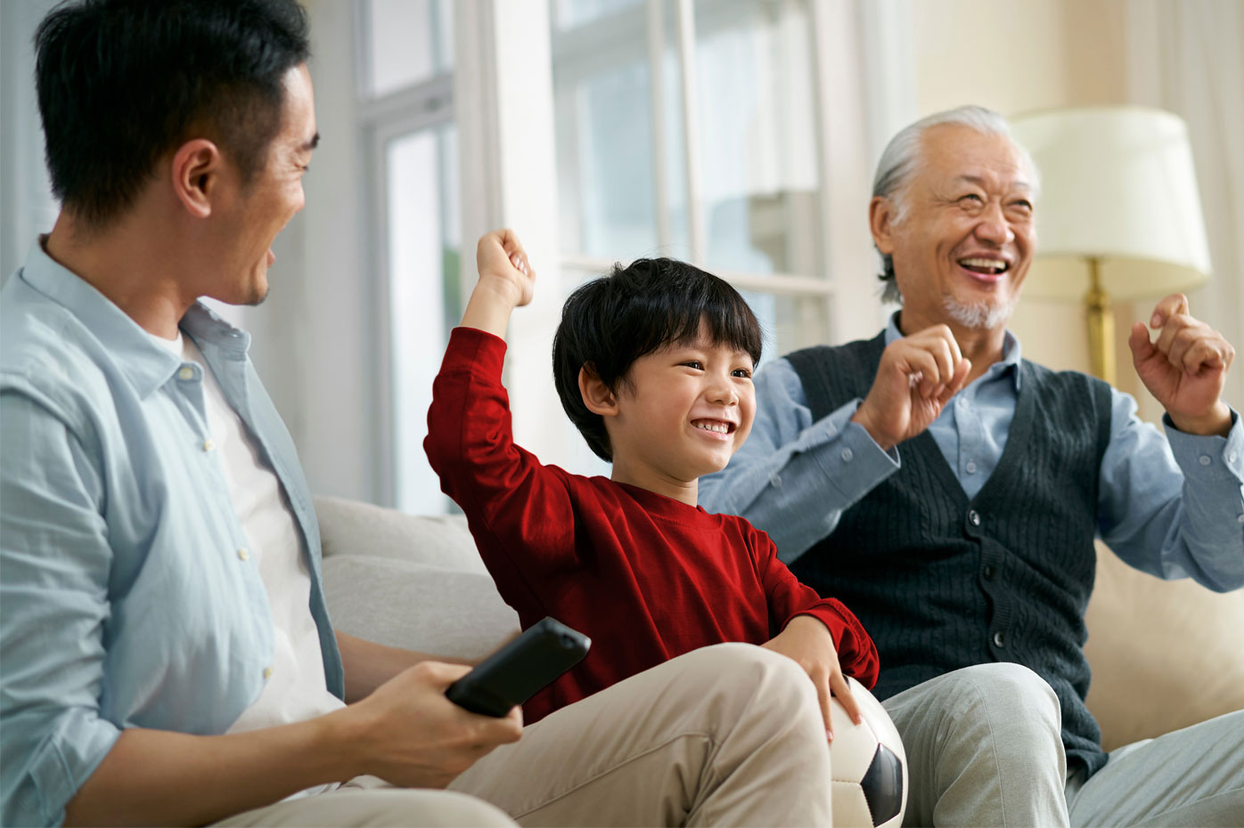 3 generations of an Asian family cheers watching a sports match on television