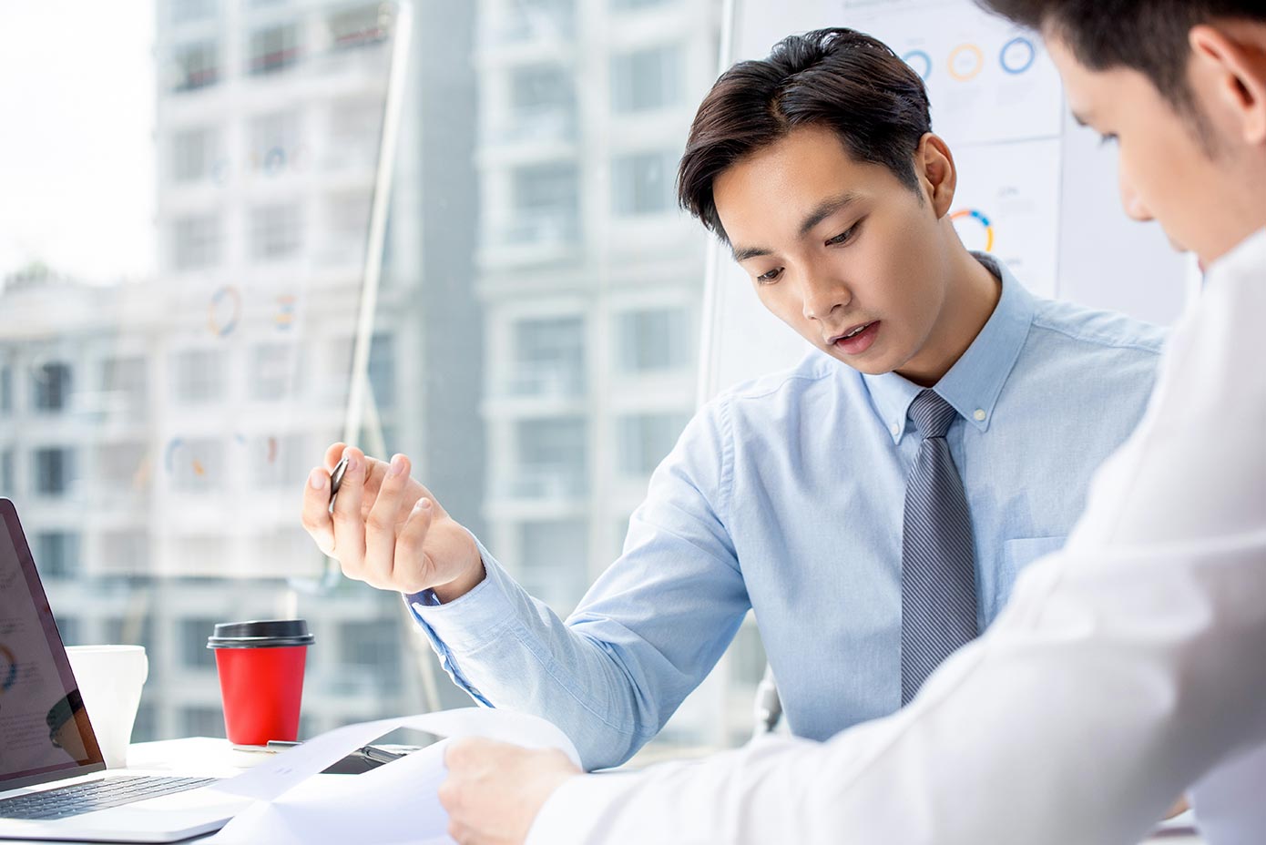 Two men in business attire working on a project with buildings in background