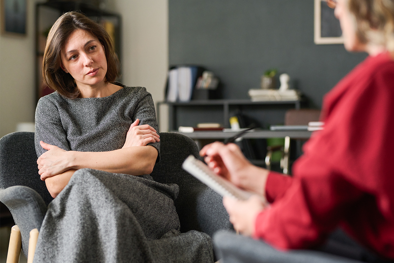 A woman crosses her hands over her chest and gazes ahead at an analyst taking notes