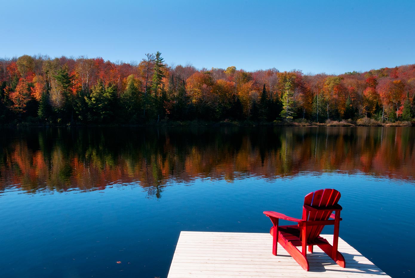 Red Adirondack chair on a dock looking over a lake