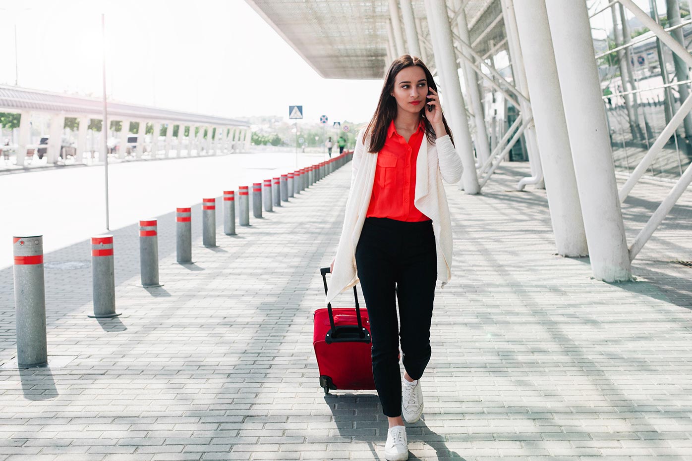 A woman on the phone with a red suitcase at the airport