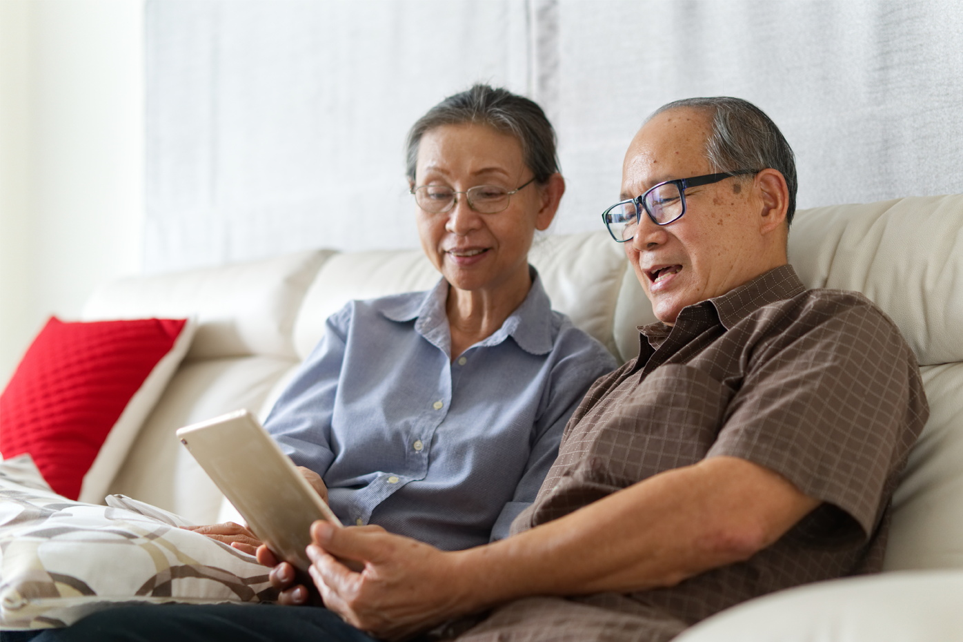 A senior couple relaxes on the couch, looking at a tablet