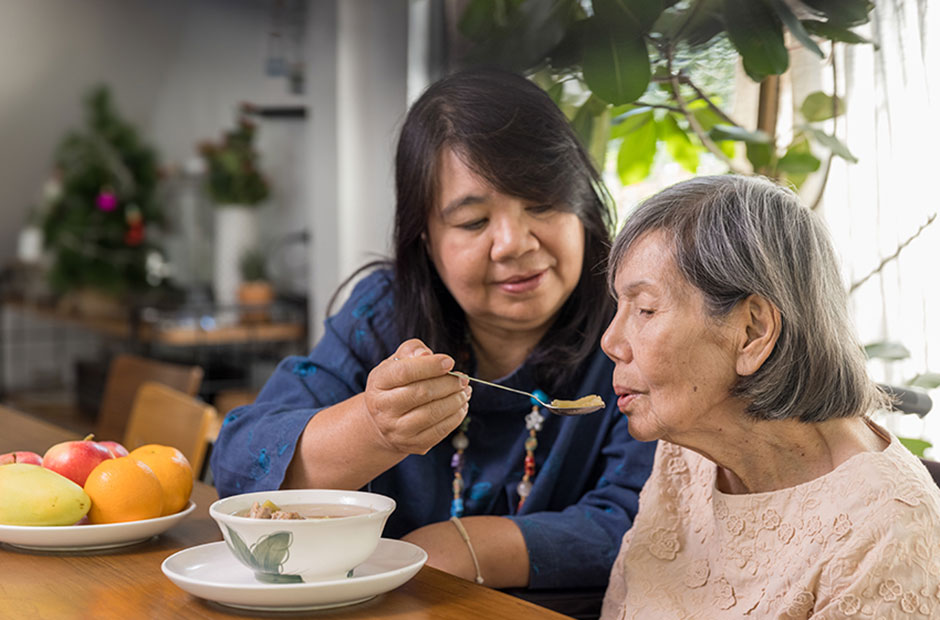 A caregiver gently feeds an elderly woman