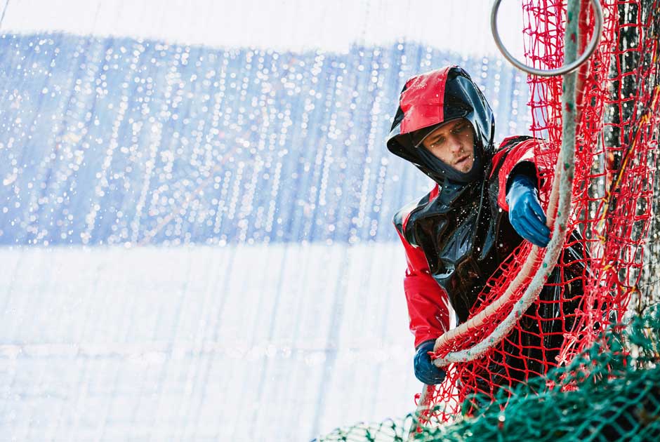 A sailor hauls a red net to check his catch amid a rainstorm.