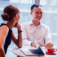 Two Asian people sitting at desk with a laptop