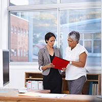 Two women standing and looking at red folder